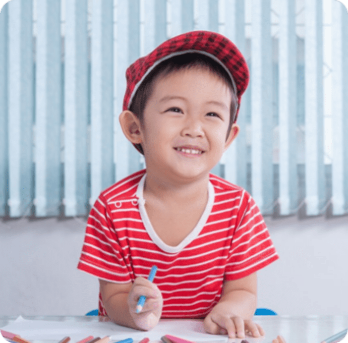 a preschooler similing holding a pencil in one of the best preschools in los angeles county